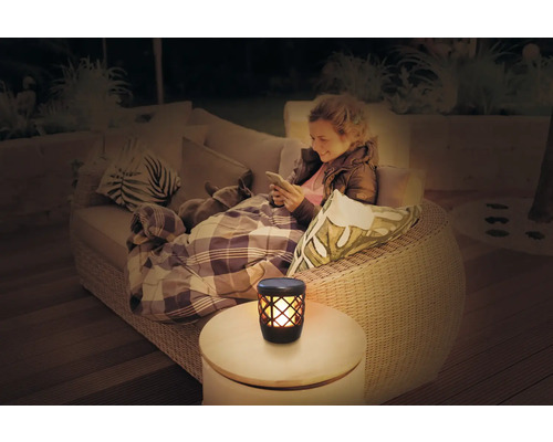 Vrouw ontspant met hond op de bank in de tuin, naast haar een tafellamp met vlameffect.