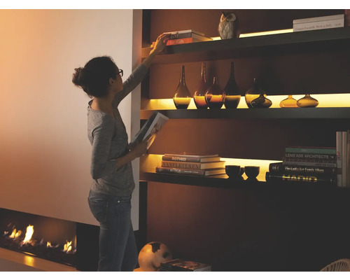 Vrouw ordent boekenkast met verlichting naast open haard