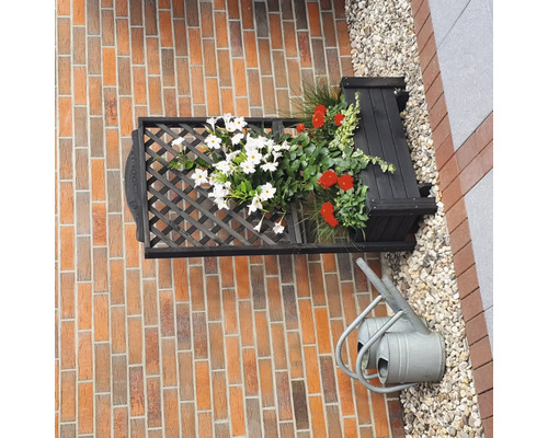 Aan de muur gemonteerde beplante bloembak met rooster en gieter voor een bakstenen muur