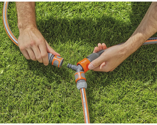Twee handen verbinden een tuinslang met een Y-stuk op een gazon.