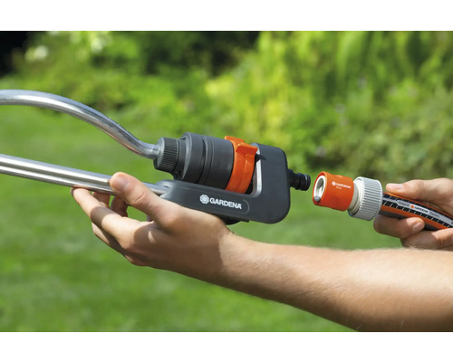 Persoon verbindt een tuinslang met een sproeier van Gardena.