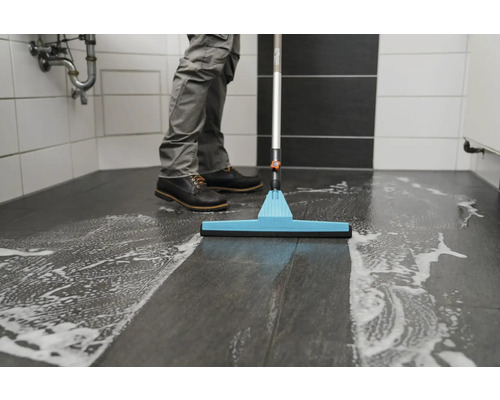 Schoonmaker maakt badkamervloer schoon met reinigingsmiddel en vloertrekker