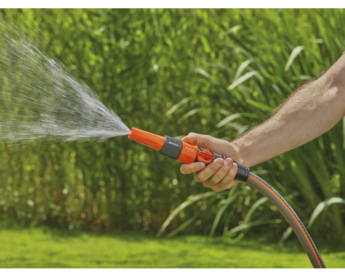Een persoon houdt een tuinslang met sproeikop vast waar water uit komt.