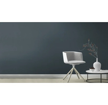 Woonkamer met stoel, tafel en decoratie voor een donkere muur.
