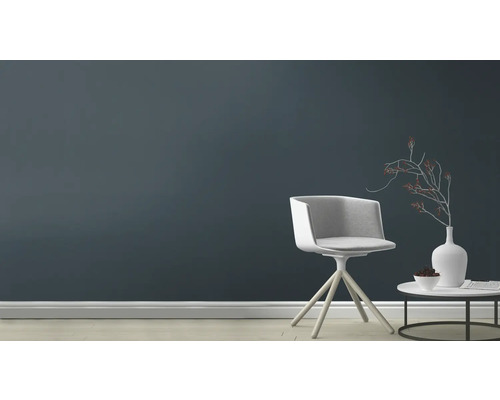 Woonkamer met stoel, tafel en decoratie voor een donkere muur.