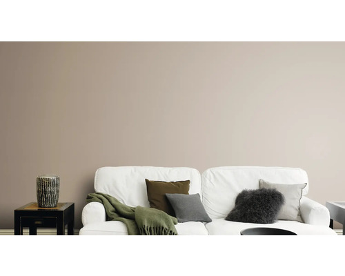 Woonkamer met witte bank, kussens, deken en decoratieve vaas op een bijzettafel voor een effen muur