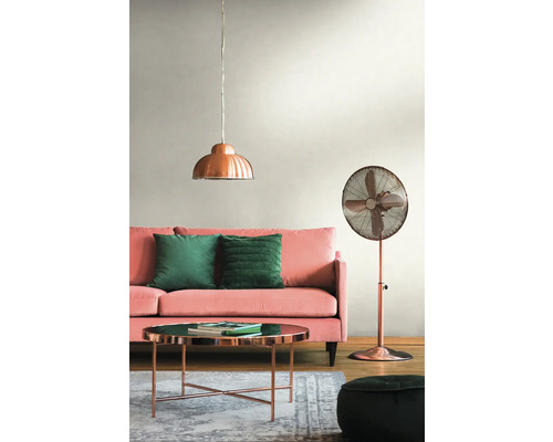 Woonkamer met roze bank, groene kussens, koperkleurige tafel, staande lamp en hanglamp.
