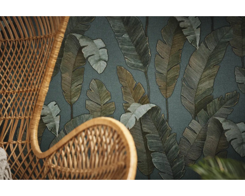 Close-up van een rotan stoel tegen een achtergrond van behang met bladerpatroon.