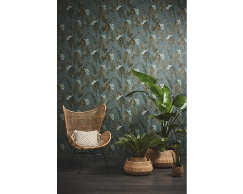 Woonkamer met rotan stoel, planten en een behang met bladerenpatroon