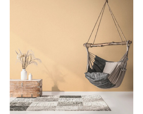 Hangstoel met kussens, vloerkleed met patroon en houten kist met vazen in een lichte kamer.