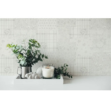 Decoratieve scène met gemust behang, eucalyptus takken in een metalen kan, kaars en cement konijn op een wit dienblad.