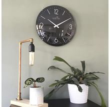 Decoratieve scène met een zwarte wandklok, een koperen tafellamp en twee kamerplanten in potten.