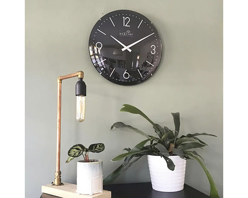 Decoratieve scène met een zwarte wandklok, een koperen tafellamp en twee kamerplanten in potten.