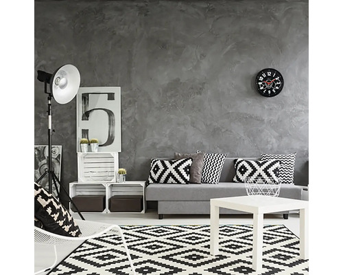 Woonkamer met grijze muur, bank met kussens, tapijt met geometrisch patroon en witte salontafel.