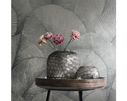 Twee vazen en bloemen op een tafel voor een muur met behang met bladmotief.