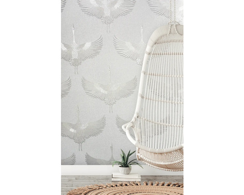 Scene met een witte hangstoel voor een behang met kraanvogelmotief.