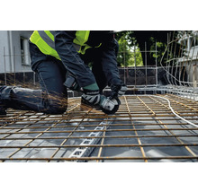 Een vakman knielt op een bouwplaats en snijdt met een Metabo haakse slijper stalen balken, waarbij vonken vliegen.