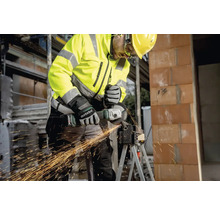 Een bouwvakker met beschermende kleding gebruikt een haakse slijper om metaal te snijden.