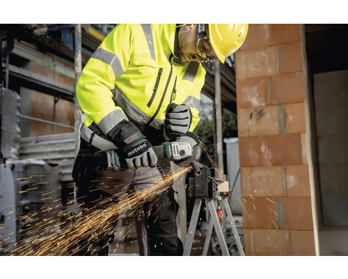 Een bouwvakker met beschermende kleding gebruikt een haakse slijper om metaal te snijden.
