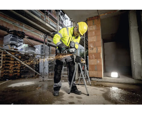 Een bouwvakker in werkkleding gebruikt een haakse slijper op een bouwplaats
