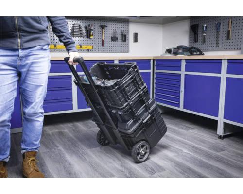 Een persoon trekt een gereedschapskofferwagen met gereedschapskisten in een werkplaats.