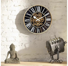 Decoratieve wandklok met Romeinse cijfers en zichtbaar uurwerk naast een Boeddhabeeld en een lamp
