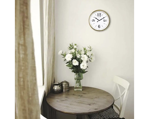 Licht interieur met een ronde houten tafel, een vaas met witte bloemen en een wandklok