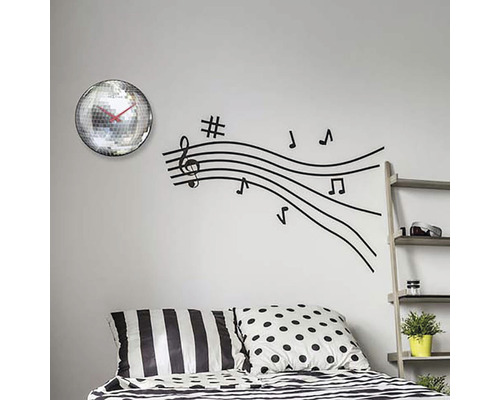 Wanddecoratie met spiegelbolklok en muzieknotenlijnen muursticker boven een bed.