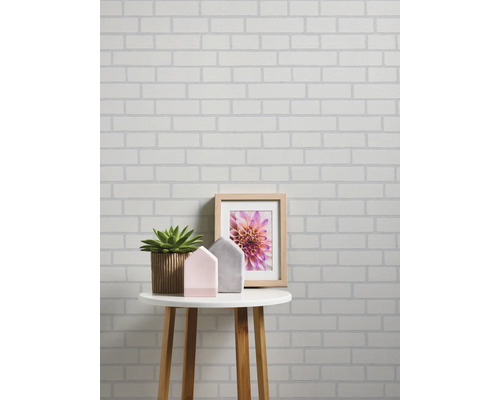 Wand met witte bakstenen behang, gedecoreerd met plant, huisjes en fotolijst op een tafel