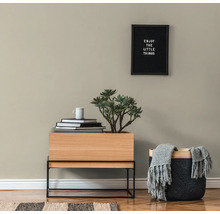 Woonkamerscène met een houten tafel, een plant, boeken, een beker, een mand met een deken en een ingelijst citaat aan de muur.