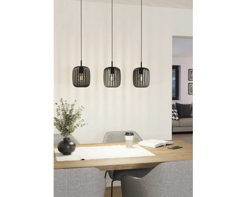 Drie metalen hanglampen hangen boven een eettafel en geven licht.