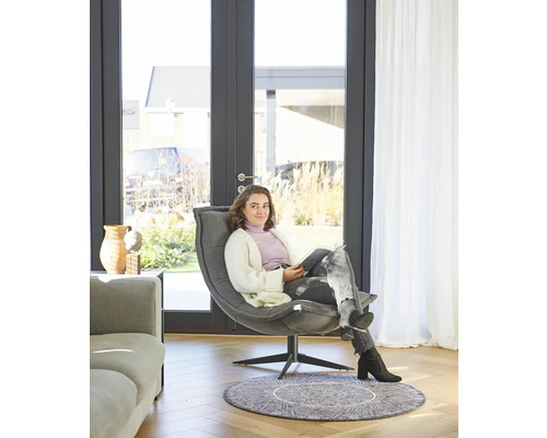 Een vrouw zit in een stoel voor een terrasdeur in een lichte kamer.