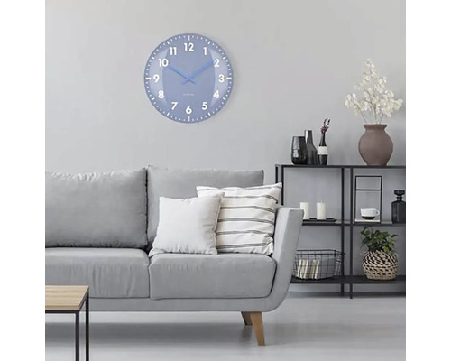 Woonkamer met grijze bank, rek en een ronde wandklok met wijzerplaat