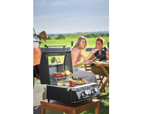 Gasbarbecue op houten tafel met groenten en vrouwen op de achtergrond