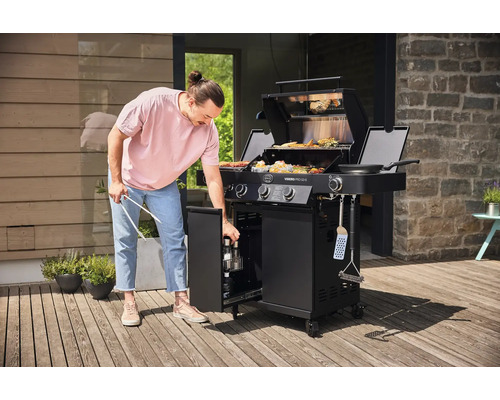 Man bedient een zwarte gasbarbecue met open opbergruimte op een terras
