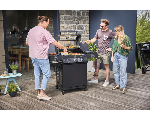 Drie mensen staan rond een zwarte gasbarbecue op een terras en grillen eten.