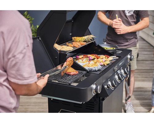 Mensen grillen vlees en groenten op een zwarte gasbarbecue in de buitenlucht.