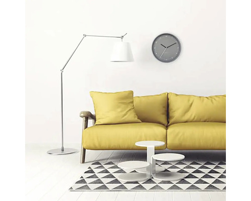 Woonkamer met gele bank, staande lamp, wandklok en tapijt met geometrisch patroon