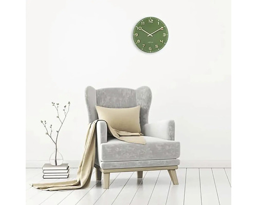 Woonkamer met groene wandklok, fauteuil, kussen en deken.