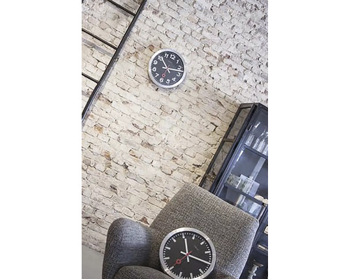 Woonkamer met bakstenen muur, ladder, vitrine, fauteuil en twee klokken