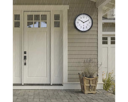 Scène met een ronde, weerbestendige buitenklok naast een voordeur tijdens een regenbui.