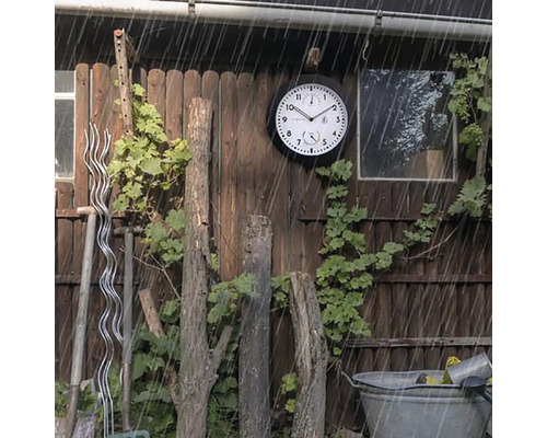Tuinscene met een weerbestendige buitenklok aan een houten muur in de regen.