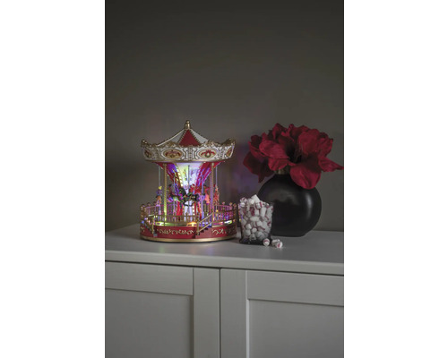 Decoratieve carrousel met verlichting, naast een glas marshmallows en een vaas met bloemen op een kast