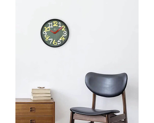 Wandklok met wijzerplaat en cijfers boven een houten kast en een stoel