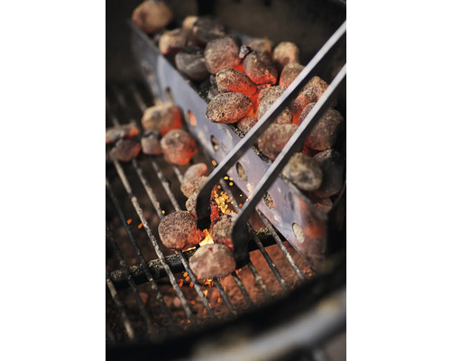 Grilltang hanteert gloeiende grillkolen in een aanmaakkorf op een grillrooster.