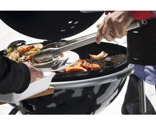 Barbecue met voedsel en barbecue gereedschap in gebruik.