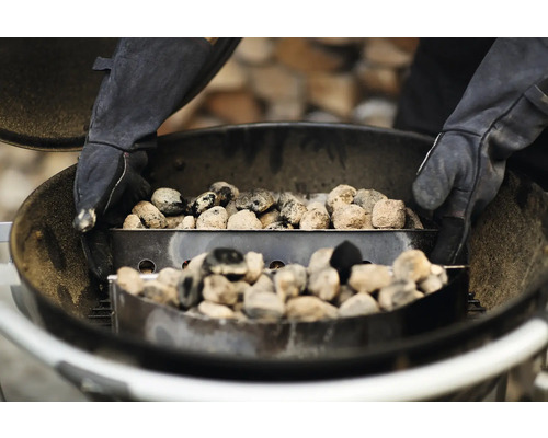 Barbecue met briketten en een persoon met handschoenen