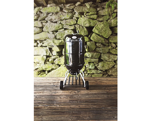 Zwarte bolvormige barbecue met wielen voor een stenen muur