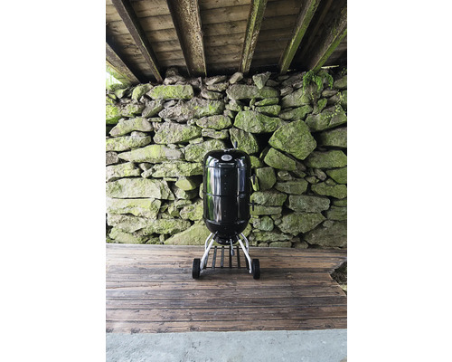 Zwarte bolvormige barbecue met wielen voor stenen muur
