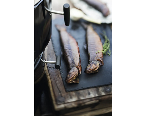 Gerookte forel op een leistenen bord naast een barbecue